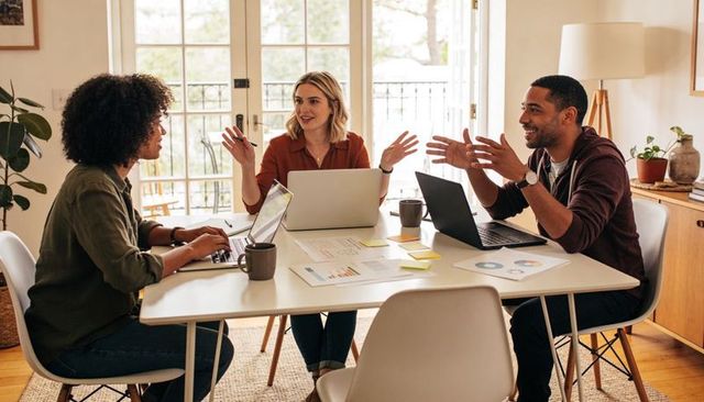 Remote team collaborating around table with laptops, charts, coffee in home office