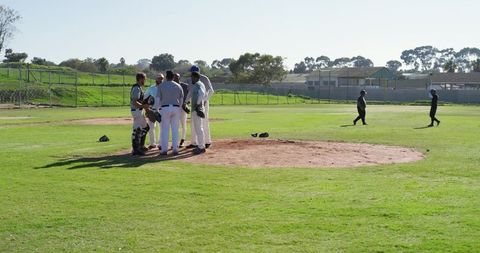 Diverse male baseball team huddling on pitcher's mound at sunny community ballpark