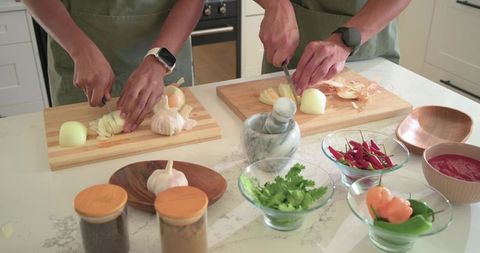 African american couple chopping onions and garlic on marble kitchen counter wearing green aprons