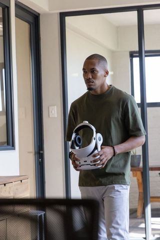 African american man holding white vr headset in modern glass office workspace daylight