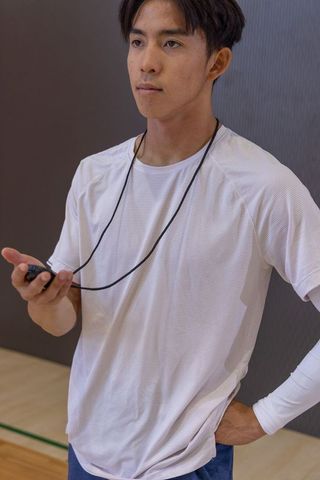 Asian coach holding stopwatch on hardwood court, focused fitness training and precise timing