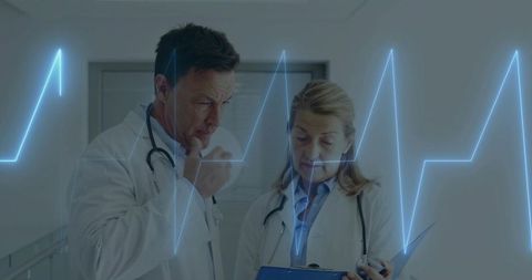 Two physicians reviewing ECG results on clipboard in clinical corridor discussing cardiac care