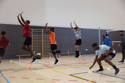 African american teen athletes practicing agility drills over hurdles in school gym