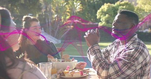 Friends chatting at outdoor picnic, man in plaid gesturing during casual lunch