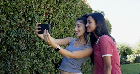 Cheerful female friends taking selfie with smartphone outdoors