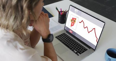 Woman studying nft market on laptop with falling red chart and buy button at desk