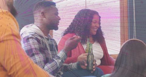 Friends laughing and chatting during cozy casual hangout on sofa holding bottles