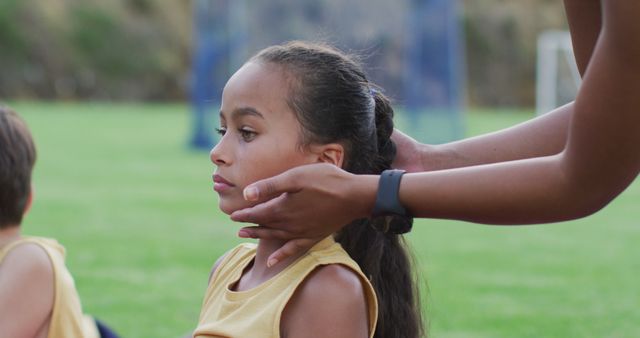 Coach adjusting young girl's hair during outdoor sports practice, highlighting care and preparation for the children. Can be used in contexts related to sports coaching, team preparation, children's activities, teamwork, and outdoor exercises.