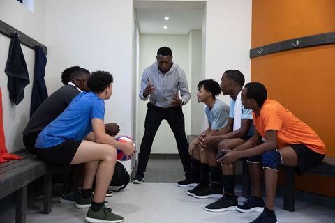 African american coach motivating teenage volleyball team in locker room huddle
