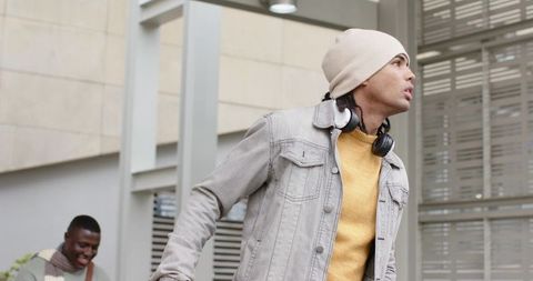Urban friends walking with headphones and beanie near modern building, casual street style