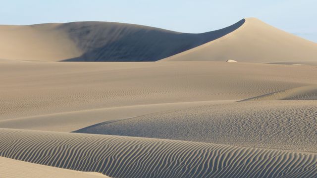 Rolling sand dunes create a serene and minimalistic desert landscape. Ideal for nature and travel-related uses, websites focusing on the environment, or as a peaceful decor image. The untouched and vast sand formation symbolizes tranquility and untouched wilderness.