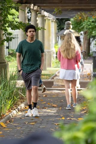 Young people walking through garden pergola pathway with stone columns and autumn leaves