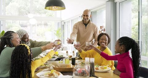 Multigenerational family raising glasses and enjoying brunch around sunlit modern table