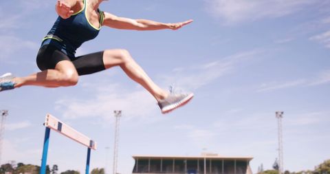 Athletic woman jumping over hurdle on track