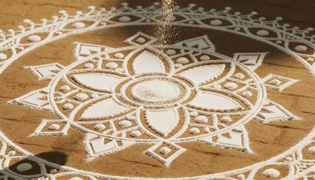 Pouring white powder over geometric rangoli mandala on packed brown sand
