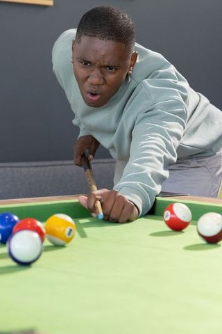 African american male lining up pool shot with cue stick on green felt in game room