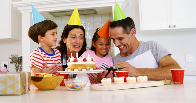 Family celebrating a birthday at home with a cake and party hats. They are enjoying time together, creating joyful memories. This image is ideal for use in articles, advertisements, or family-oriented designs that emphasize happiness, special moments, and family bonds.