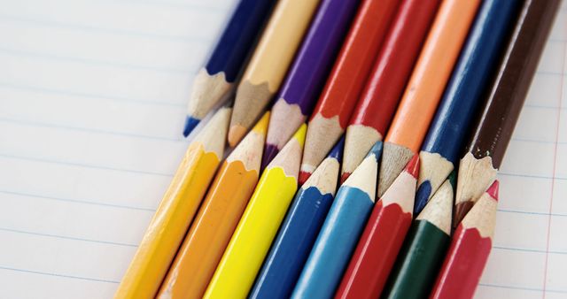 Various colored pencils laid out diagonally on lined notebook paper. Useful for illustrating concepts related to creativity, education, art projects, and back-to-school themes. Great for advertisements for school supplies, educational content, and artistic endeavors.