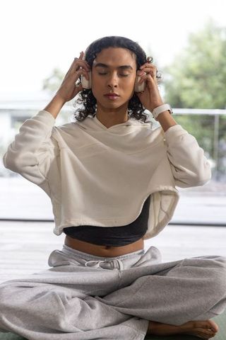 Young woman meditating with headphones on balcony wearing cropped hoodie and smartwatch