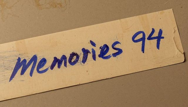 Vintage yellowed label handwritten memories 94 blue ink closeup on cardboard texture aged