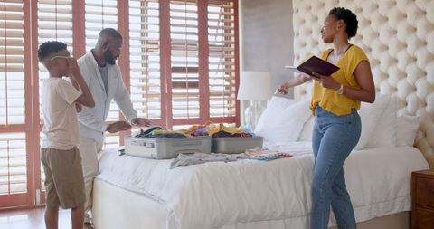 African American family packing for vacation in sunlit bedroom, organizing suitcase