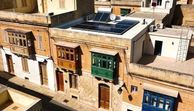 Sunlit mediterranean stone facade with colorful wooden balconies and rooftop solar panels