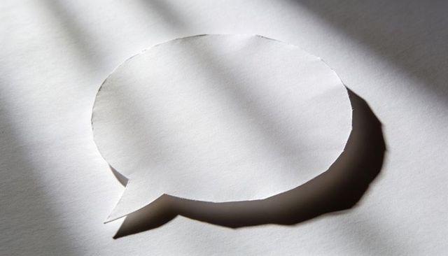 Paper speech bubble casting bold shadow on textured paper with diagonal light bands, minimal