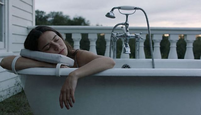 Woman relaxing in vintage freestanding bathtub on porch at dusk, outdoor relaxation
