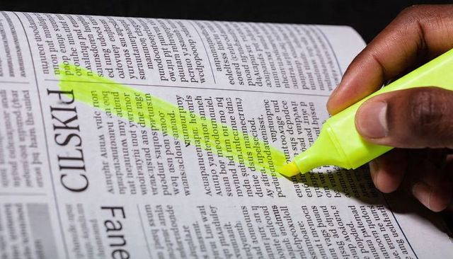 Right Hand Highlighting Newspaper Column with Yellow Highlighter Closeup for Study