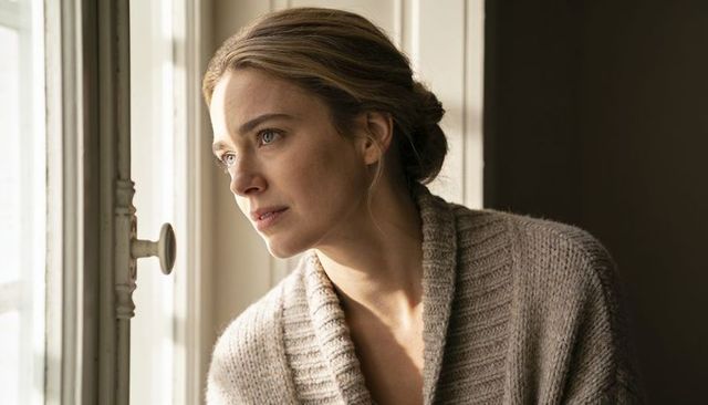 Serene woman gazing out window in knit cardigan, cozy morning light, contemplative portrait