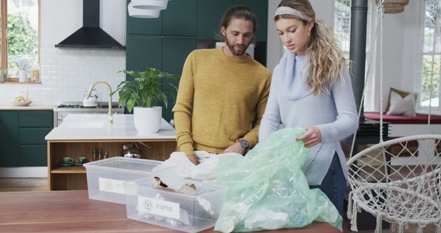 Couple is sorting waste into plastic and paper bins in a modern kitchen, emphasizing eco-friendly practices. Ideal for illustrating concepts related to sustainability, recycling efforts, and environmental conservation in a domestic setting. Useful for blogs or articles about green living, waste management systems, and household environmental initiatives.