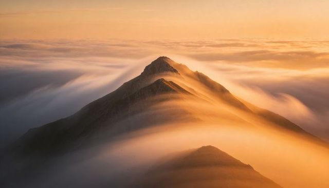 Sunlit serrated mountain ridge rising above sea of clouds at golden-hour with misty peaks