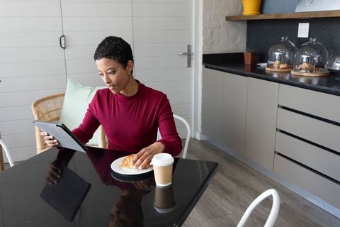 African american woman in her 30s reading tablet while enjoying morning coffee and pastry