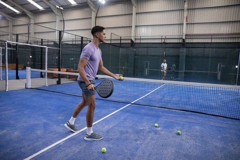 Male athlete serving on indoor blue padel court, holding paddle and tennis ball