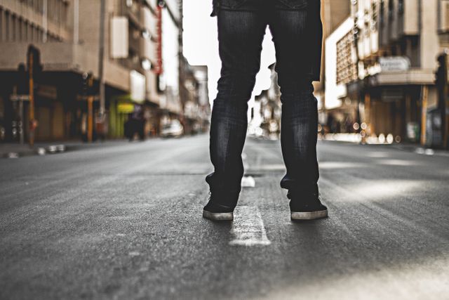 Person standing in empty urban street in jeans and sneakers - Download Free Stock Photos Pikwizard.com