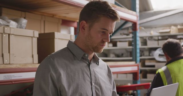 Warehouse worker holds tablet for inventory management in a storage facility. Ideal for use in articles about warehouse operations, logistics, modern technology in industrial settings, and supply chain management.