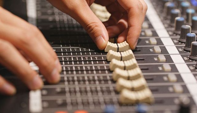 Hands adjusting white faders on audio mixing console close-up for music production