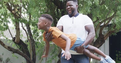 Joyful African American Father Playing with Son Outdoors in Sunny Backyard