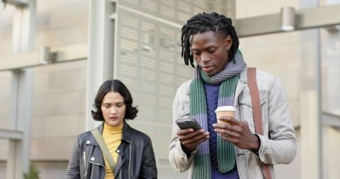 Diverse commuters walking in transit hub using smartphone and holding takeaway coffee