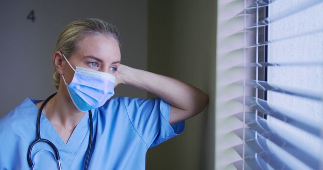 Portrait of caucasian female doctor wearing face mask looking through the window in hospital room. medicine, health and healthcare services during coronavirus covid 19 pandemic.