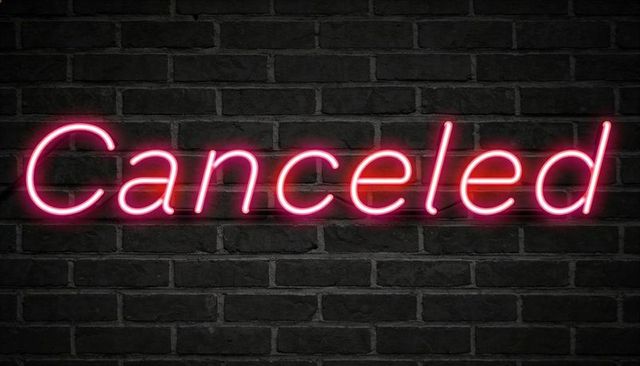 Glowing pink neon canceled sign casting magenta halo on dark brick wall