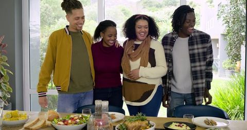 Diverse friends standing around sunlit dining table sharing home-cooked feast and laughter