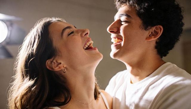 Couple laughing and leaning close in warm studio, intimate candid portrait with soft glow