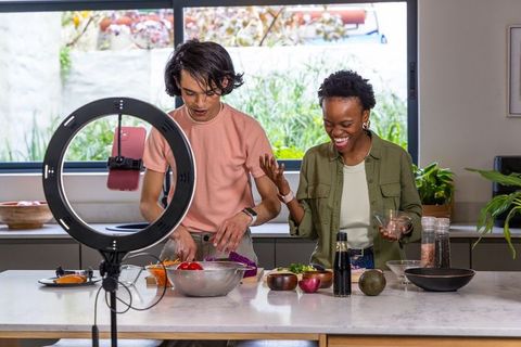Asian man and african american woman filming lively home cooking vlog at kitchen island