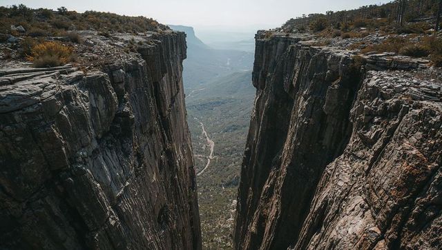 Plunging vertical canyon splitting high plateau, sheer cliffs overlooking winding valley