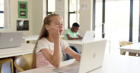 Young student concentrating on laptop in sunlit modern classroom with diverse teenage classmates