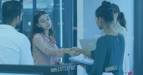 Businesswomen shaking hands in office with laptop clipboard data overlay glass reflections