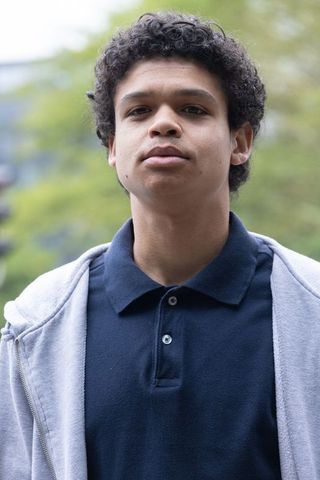 Young african american man standing on campus wearing navy polo and gray hoodie, confident
