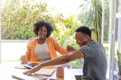 African american couple laughing at bright dining table with coffee mugs and tablet