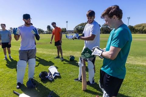 Multiracial men preparing for cricket batting practice on sunny outfield with pads